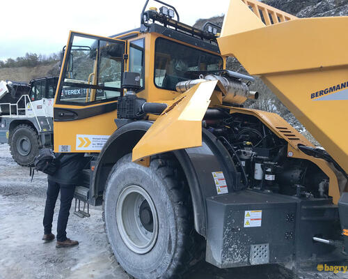 22. Otevřený kryt pro přístup k motoru a převodovce. Rám s pracovními a výstražnými světly na kabině lze sklopit pro snížení celkové výšky stroje.