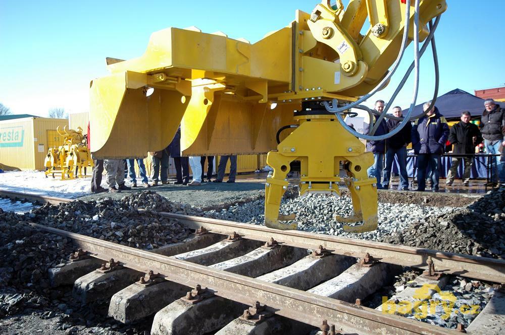 Měnič pražců Windhoff ASW - pod lžící se ukrývají otočné kleště na pražce